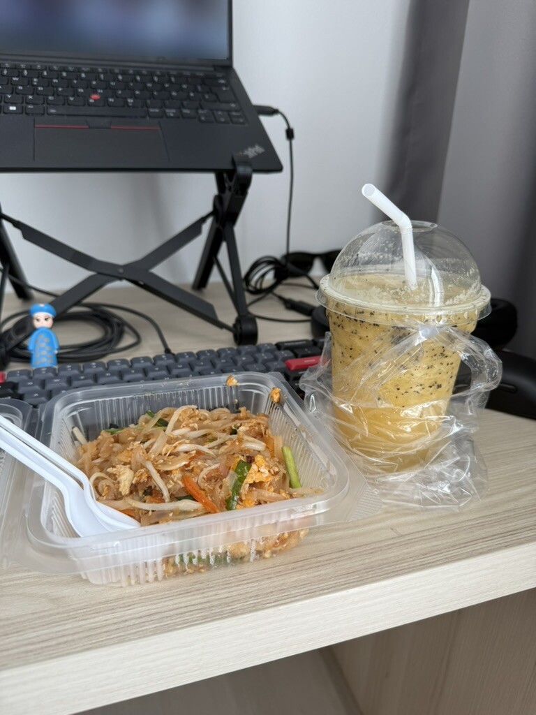 Eine Mahlzeit und ein Getränk neben Tastatur und Laptop an einem Arbeitsplatz. Der sichtbare Bildschirm ist unkenntlich gemacht.