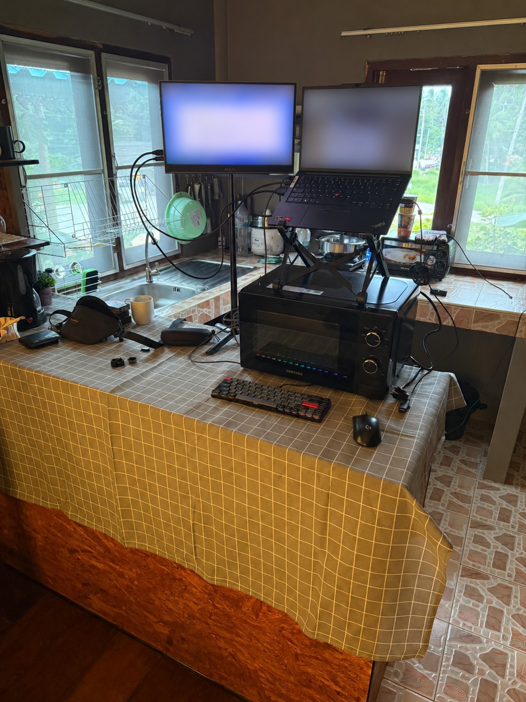 Laptop und zweiter Monitor auf einer hohen Küchenfläche auf Ko Pha Ngan. Unter der Arbeitsfläche fehlt Beinfreiheit; beide Bildschirminhalte sind unkenntlich gemacht.